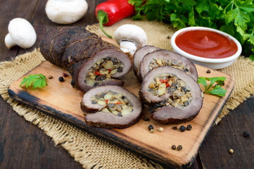 Meatloaf (roll) stuffed with mushrooms, sweet pepper and tomato sauce on a dark wooden background. Festive dish