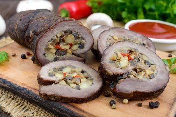 Meatloaf (roll) stuffed with mushrooms, sweet pepper and tomato sauce on a dark wooden background. Festive dish