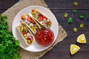 Tacos - wheat tortilla with meat, vegetables, greens and corn with tomato sauce on a dark wooden background. Traditional Mexican cuisine.