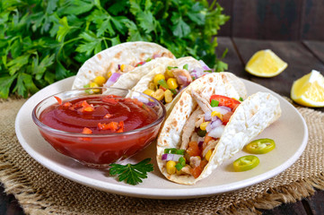 Tacos - wheat tortilla with meat, vegetables, greens and corn with tomato sauce on a dark wooden background. Traditional Mexican cuisine.