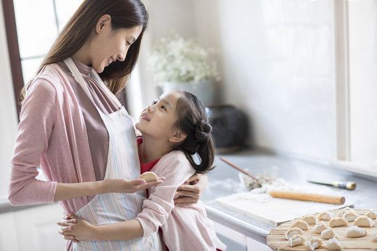 Cheerful mother and daughter making dumplings in kitchen