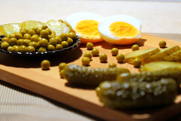 Ingredients for salad - chicken eggs, canned green peas in a black plate and appetizing pickled cucumbers.