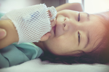 Illness asian child admitted in hospital with saline iv drip on hand.