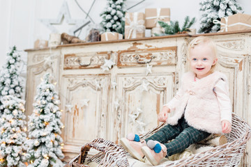 portrait beautiful little girl near old vintage chest of drawers. Christmas tree decoration and light bulbs garlands