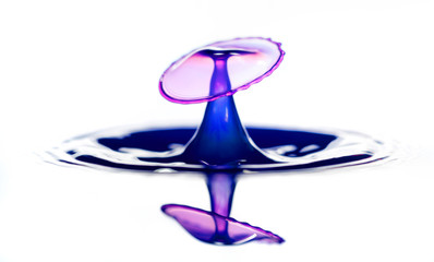 Splash and crown on rippled blue liquid or water surface . Water splash with a crown and reflection