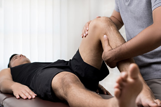 Therapist treating injured knee of athlete male patient in clinic