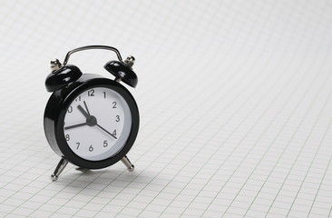 Black alarm clock isolated on white checkered background