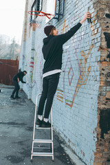 man standing on ladder and painting colorful graffiti on building