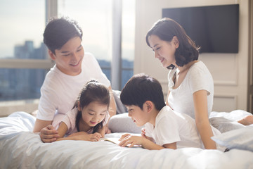 Cheerful young family reading a book on bed