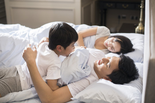 Cheerful boy waking up his parents in bedroom