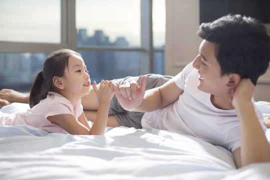Cheerful young father making a pinky swear with his daughter on bed