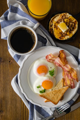 American breakfast with sunny side up eggs, bacon, toast, pancakes, coffee and juice