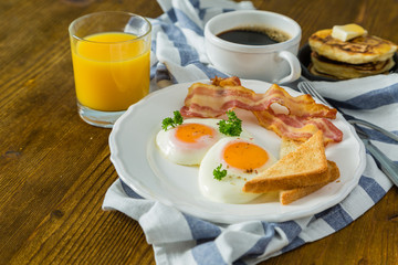 American breakfast with sunny side up eggs, bacon, toast, pancakes, coffee and juice