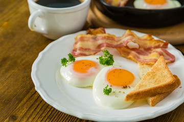 American breakfast with sunny side up eggs, bacon, toast, pancakes, coffee and juice