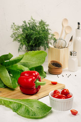 Healthy vegetarian ingredients for spring fresh green salad and kitchenware in white wooden kitchen interior. Spring vitamin dieting food.