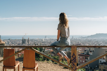 Rear view of young woman wearing in stripped t-shirt sitting on high point and looking at...