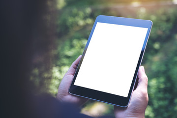 Mockup image of woman's hands holding black tablet pc with blank white screen and green nature background