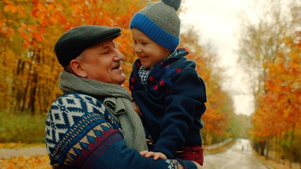 Little happy boy and his grandfather are smiling in the autumn park