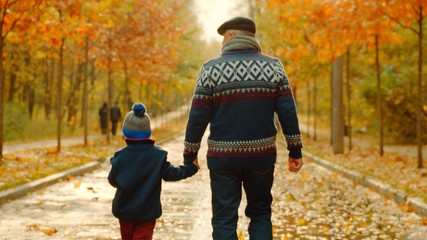 Little boy and his grandfather are walking in the autumn park