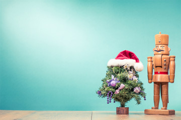 Christmas tree in Santa's hat and retro wooden nutcracker toy on table front aquamarine wall...