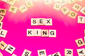 Wooden blocks on a pink background spelling words Sex King
