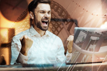 Great achievement. Overjoyed young man raising his fists in triumph and screaming happily while having a video call and hearing perfect news