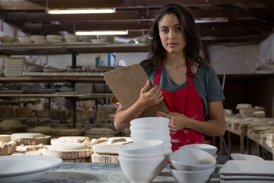 Confident female potter standing with clipboard
