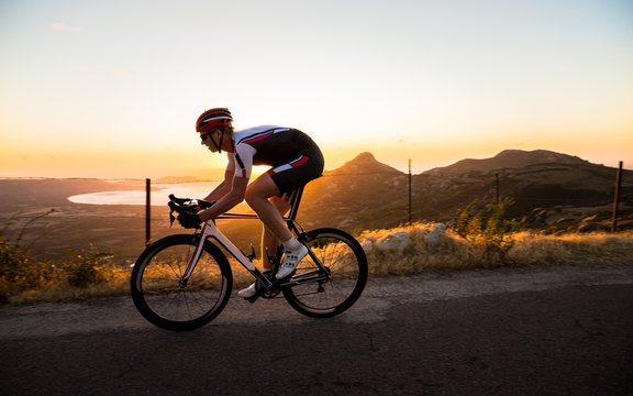 A cyclist does road biking at sunset above the shoreline in Corsica, France.