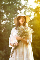 Beautiful sunny girl / woman in white dress and straw hat with bouquet of wildflowers - 185234854