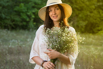 Beautiful sunny smiling girl / woman in white dress and straw hat with bouquet of wildflowers - 185234881