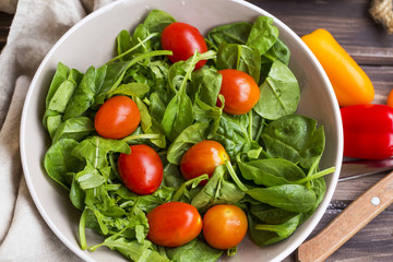 Spring salad closeup with fresh green rocket, spinach leaves and cherry tomatoes , top view