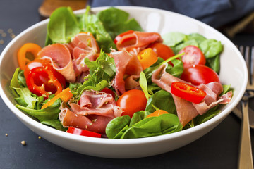 Fresh prosciutto ham and vegetables salad with spinach , tomatoes , peppers and ham seasoned with herbs, top view, healthy spring salad