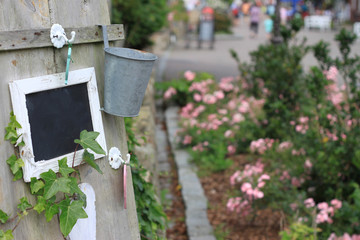 romantischer Garten mit kleiner Schiefertafel im Vordergrund und mit rosa Rosen und Fußgängerzone verschwommen im Hintergrund.Where: Norddorf, Amrum.When: 03.08.2013.