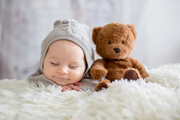 Foto op Plexiglas Lieve babyjongen in berenoverall, slapend in bed met teddybeer © Tomsickova
