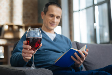 Take it. Silhouette of smiling man that expressing positivity while reading book and going to drink wine