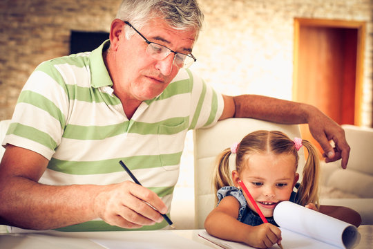 Grandfather Painting A Book With Granddaughter.