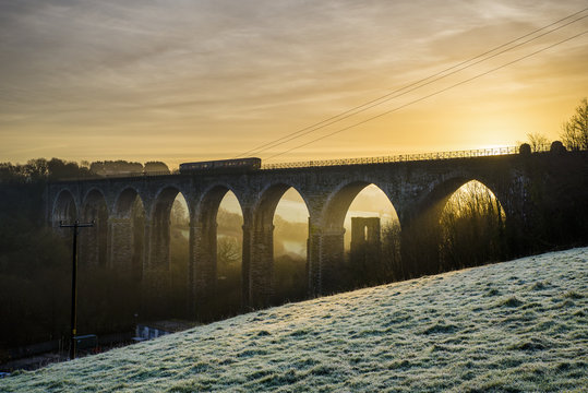Viaduct on a frosty morning with a beautiful golden sunrise and a train travelling across, moorswater, liskeard. cornwall, uk