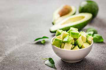 Ripe avocado cubes in a bowl on concrete background. Selective focus, space for text. 