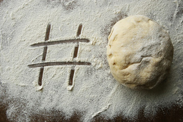 Hashtag written in flour and raw ball of dough. Number sign on floured wooden surface and fresh yeast dough for baking.