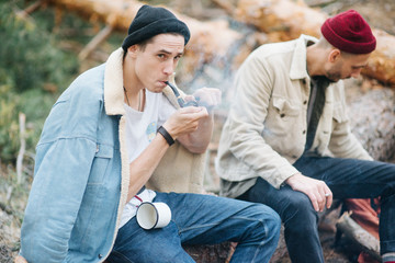 Smoke from a cigarette with blurred men on a natural background. Summer camping, hiking, vacation concept.