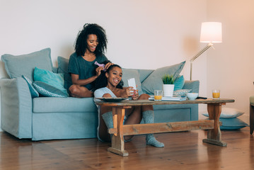 Happy young two black women sitting in the couch combing the hair .