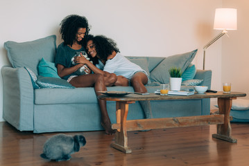 Happy young two black women sitting in the sofa giving affection to a bunny .