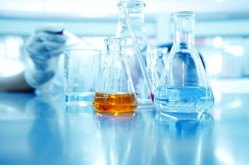 hand of scientist or reseracher drop solution in glass beaker and orange liquid in  flask at...