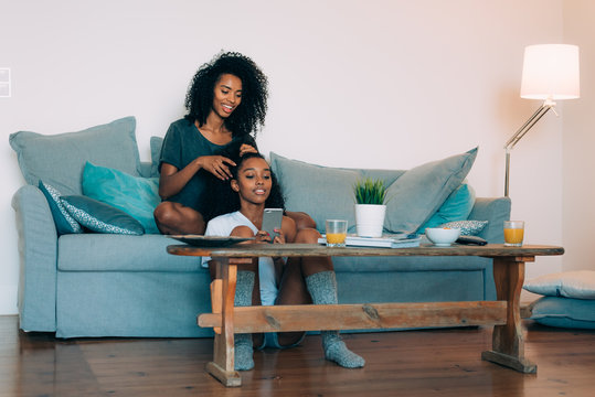 Happy Young Two Black Women Sitting In The Couch Combing The Hair .