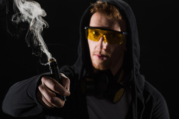 Man wearing protective glasses vaping electronic cigarette isolated on black