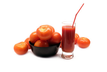 Big glass with tomato juice with drinking strawand many ripe tomatoes in round black bowl studio shot isolated on white background