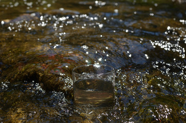 Glass of pure water in a fast mountain stream in summer