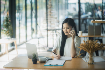 Portrait of an attractive young woman holding her phone while working in coffee shop.	