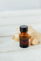 Ginger essential oil in glass bottle with ginger root behind.