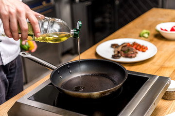 cropped image of chef pouring oil on frying pan